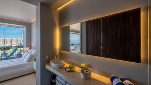 Une salle de bain moderne avec un grand miroir, un lavabo blanc et une vue sur le paysage urbain.