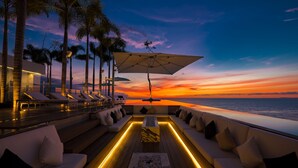 Une vue sur le coucher de soleil depuis une terrasse équipée de chaises longues et d’une piscine.