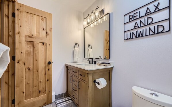 Un baño con puerta de madera, un lavabo con espejo y un cartel que dice "RELAX AND UNWIND".