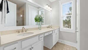 A modern bathroom with a large mirror, two sinks, and a potted plant.