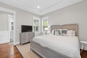 A bedroom with a wooden bed, a dresser, a TV, and a window with blinds. - Stay Where You’re Cared For—NatureWalk Seagrove w/ Zero-Entry Pool & 4 Bikes (Santa Rosa Beach)