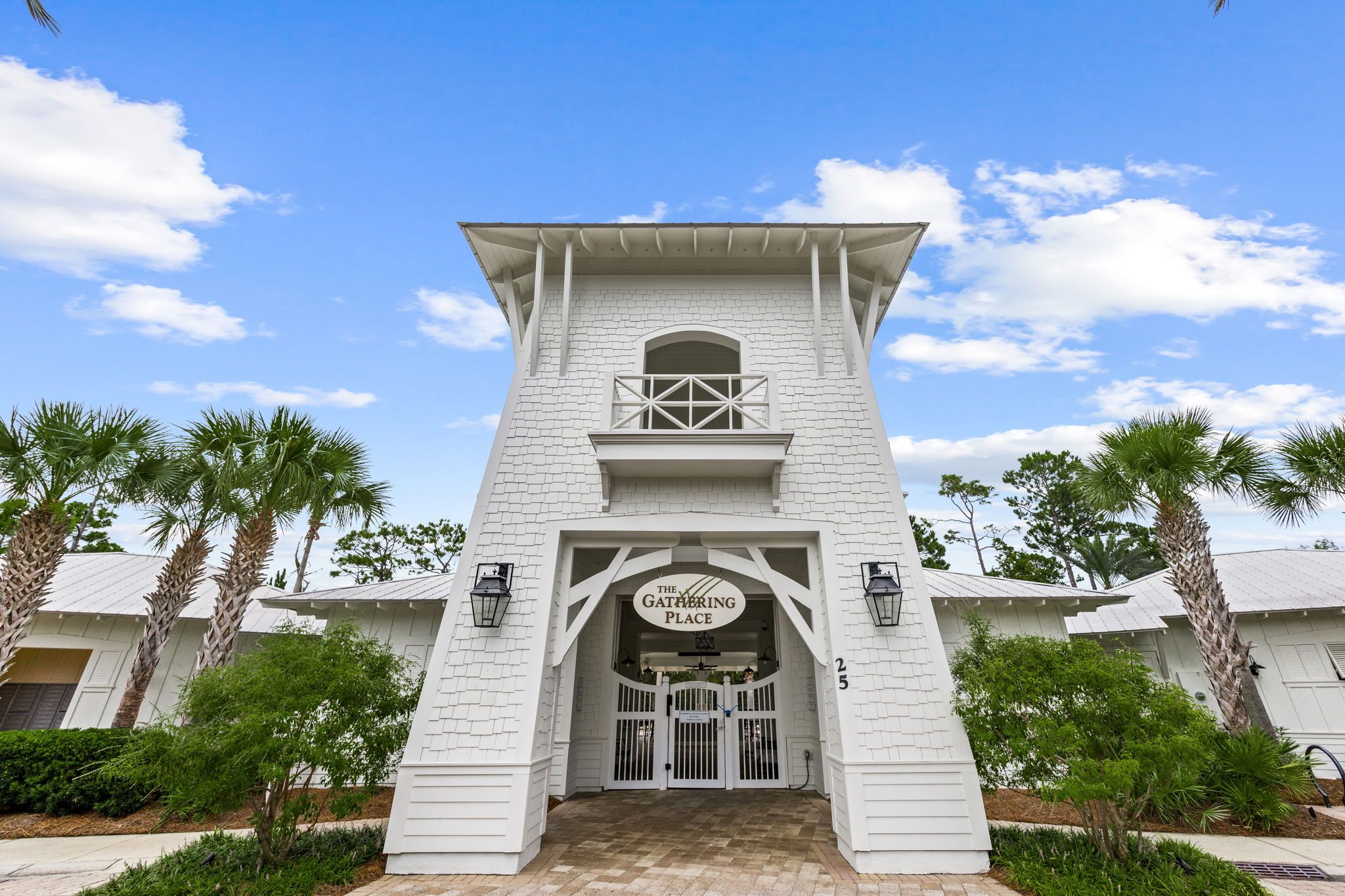 A white building with a sign reading 'The Gathering Place' above the entrance, flanked by palm trees and a clear sky.