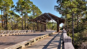 A wooden boardwalk with a covered pavilion, surrounded by tall pine trees.