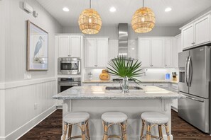 A modern kitchen with white cabinetry, a central island with stools, stainless steel appliances, and a large pendant light. - Stay Where You’re Cared For—NatureWalk Seagrove w/ Zero-Entry Pool & 4 Bikes (Santa Rosa Beach)