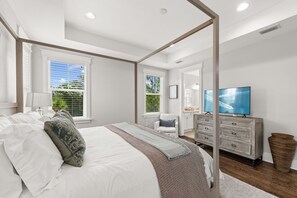 Ein modernes Schlafzimmer mit einem großen Bett, einem Schminktisch, einem Fernseher und einem Fenster mit Jalousien.