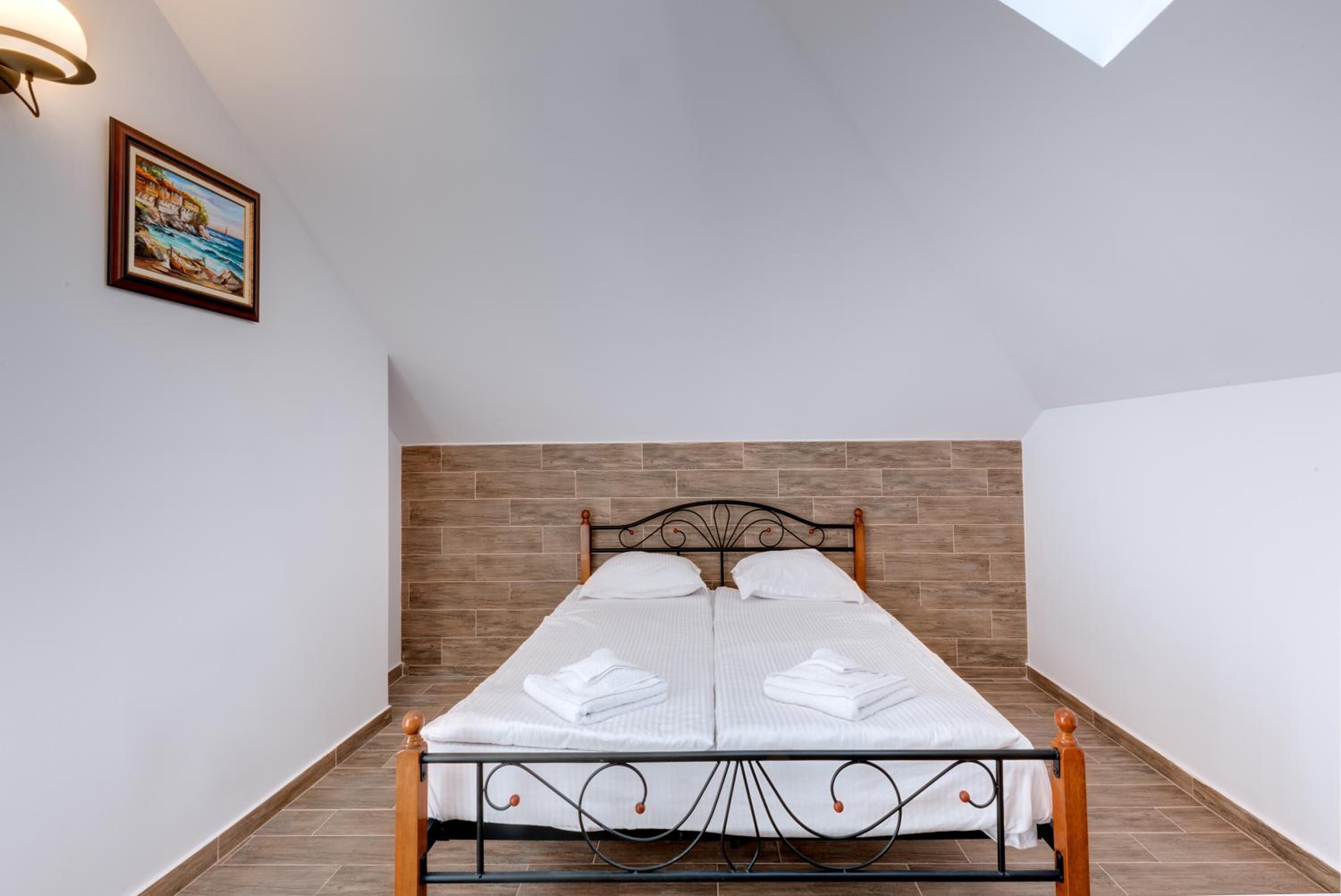 A neatly made bed with white linens and towels, a wooden headboard, and a framed picture on the wall.