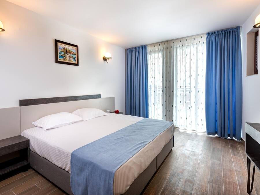 Una habitación de hotel con cama, mesita de noche y ventana con cortinas.