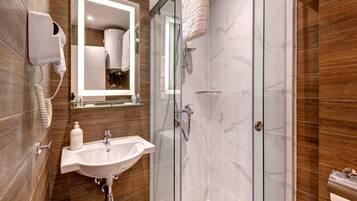 Un baño moderno con ducha envuelta en vidrio, un lavamanos con espejo y un secador de pelo montado en la pared.