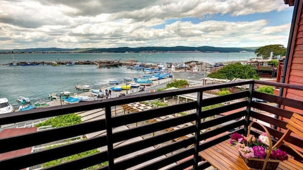 Un balcón con vista a un puerto, barcos y una costa lejana.