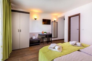 A hotel room with a bed, a desk, a chair, a TV, and a wardrobe.