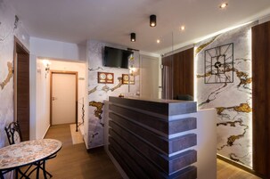Un moderno vestíbulo de hotel con una mesa de recepción, un televisor montado en la pared y un revestimiento de pared con diseño de mármol.
