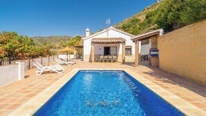 A swimming pool with lounge chairs, a patio area, and a building with a tiled roof.