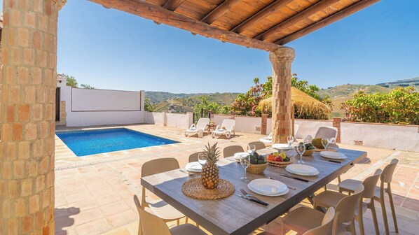 An outdoor dining area with a pool, chairs, and a table set for a meal.