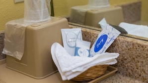A bathroom with a beige sink, a mirror, and a basket containing toiletries. - Redwood Suites (Houston)