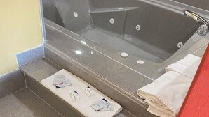 A bathroom with a bathtub, a towel rack, and a set of stairs leading to the tub. - Redwood Suites (Houston)