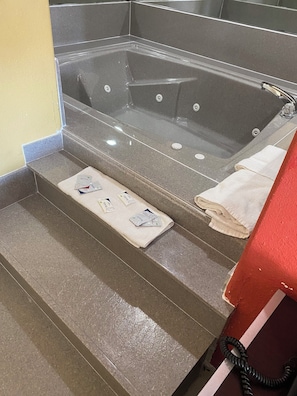 A bathroom with a bathtub, a towel rack, and a set of stairs leading to the tub. - Redwood Suites (Houston)