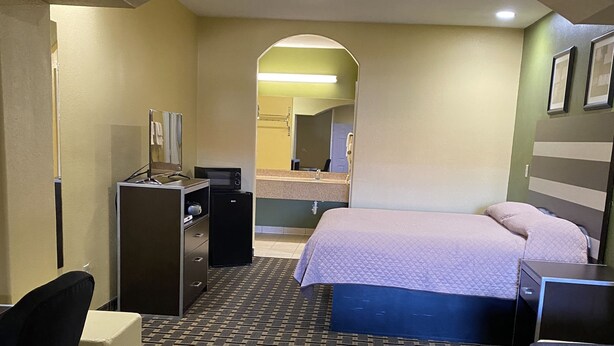 A hotel room with a bed, a desk, a chair, a small table, and a mirror. - Redwood Suites (Houston)