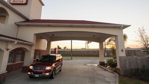 A Red Wood Suites building with a covered parking area and a maroon SUV parked in front. - Redwood Suites (Houston)