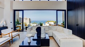 A modern living room with a large window, white furniture, and a view of the ocean. - Sail View Ocean Views, Rooftop Pool, Romantic Zone (Puerto Vallarta)