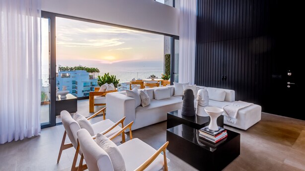 A modern living room with a large window overlooking the sea, a white sofa, and a coffee table with books. - Sail View Ocean Views, Rooftop Pool, Romantic Zone (Puerto Vallarta)