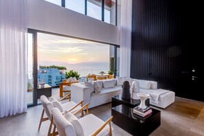 A modern living room with a large window overlooking the sea, a white sofa, and a coffee table with books. - Sail View Ocean Views, Rooftop Pool, Romantic Zone (Puerto Vallarta)