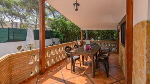 Een overdekt terras met een houten tafel en stoelen, een groene parasol en een stenen muur.