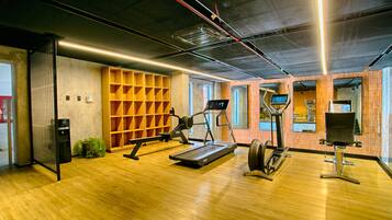 A modern gym with wooden flooring, exercise equipment, and a brick wall.