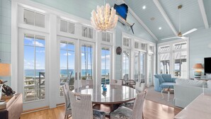 A spacious room with a large round table, wicker chairs, and a view of the ocean.