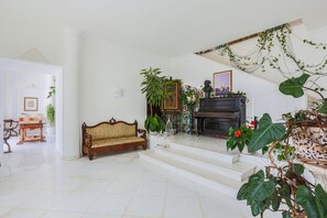 A spacious living room with a wooden sofa, a fireplace, and various plants.