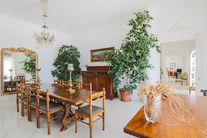 A dining room with a wooden table and chairs, a chandelier, a large mirror, and potted plants.
