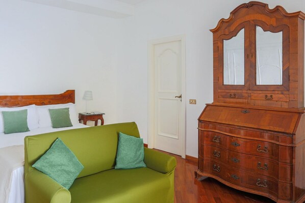 A room with a bed, a green sofa, a wooden dresser with a mirror, and a white door.
