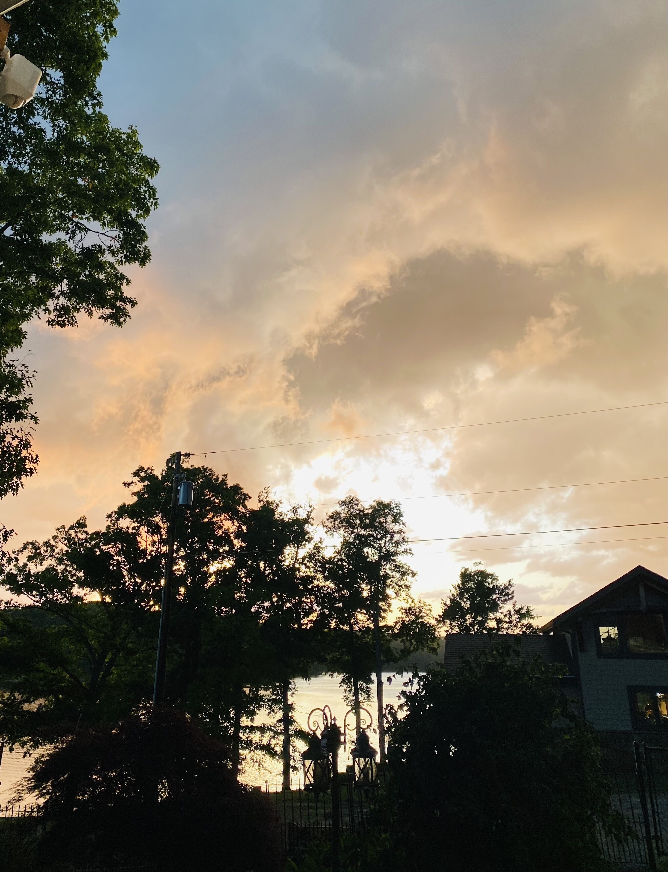 A sunset with clouds, trees, and a building in the foreground.