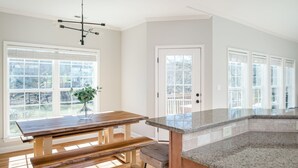 Una cocina con mesa de madera, encimera de granito y ventanas amplias.