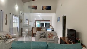 Ein geräumiges Wohnzimmer mit einer Couch, einem Fernseher und einem Essbereich im Hintergrund.