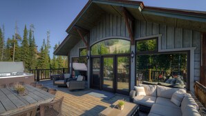 A wooden deck with outdoor furniture, large sliding glass doors, and a view of a forested area. - Grey Moose Lodge | Ski-in/Out & Hot Tub (Big Sky)