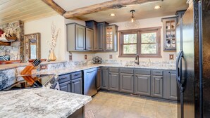 A kitchen with dark grey cabinets, a granite countertop, and a large window. - Grey Moose Lodge | Ski-in/Out & Hot Tub (Big Sky)