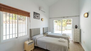 Une chambre avec deux lits, une table de chevet, une commode et une fenêtre donnant sur l’extérieur.
