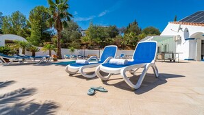 Un espace aménagé au bord de la piscine, avec des chaises longues, une piscine et un bâtiment doté d’un toit en tuiles.