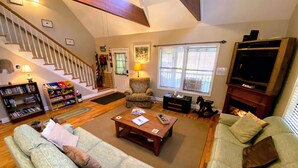 Una sala de estar amplia con una escalera, una chimenea y un televisor.