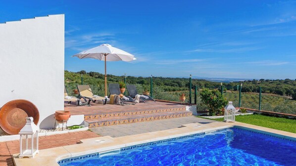 A pool area with lounge chairs, a white umbrella, and a view of the landscape.