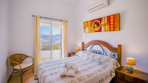 Ein Schlafzimmer mit Bett, Stuhl, Nachttisch und Fenster mit Landschaftsblick.