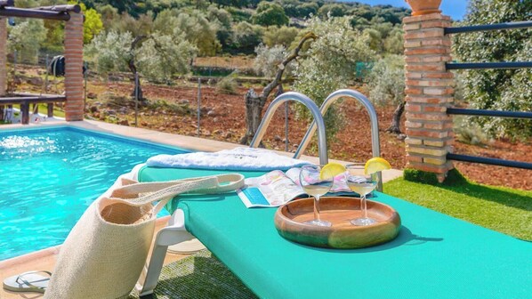 A poolside area with a lounge chair, a towel, a tray with drinks, and a pool.