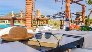 Une table avec un chapeau de paille, des lunettes de soleil, un livre ouvert, une bouteille de vin et un verre de vin.
