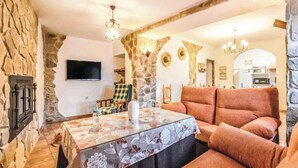 Una sala de estar acogedora con pared de piedra, chimenea, televisor, sofá y una mesa con mantel floreado.