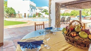 Mesa dispuesta para comer, con frutera, copas de vino y vista a una piscina y edificios.