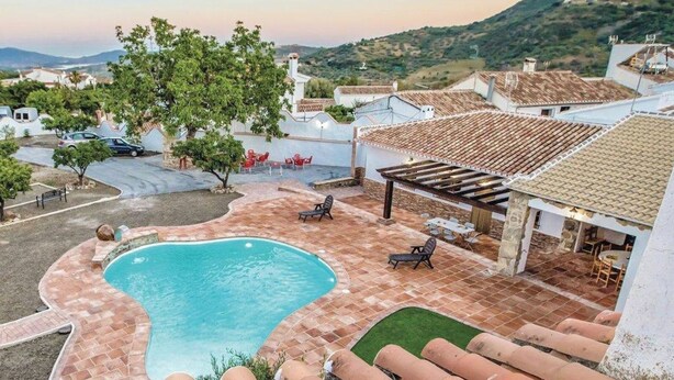 Una piscina con una pérgola y sillas de descanso, rodeada por una zona de patio con vistas al campo.