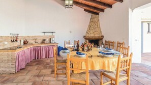 A dining area with a stone fireplace, a kitchen counter with a checkered tablecloth, and wooden chairs.
