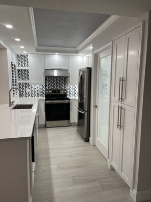 Una cocina moderna con armarios blancos, electrodomésticos de acero inoxidable y azulejos decorativos en la pared.