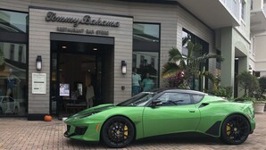 Vihreä urheiluauto on pysäköitynä rakennuksen eteen, ja rakennuksen kyltissä lukee: ”Tommy Bahama -ravintola ja -baari”.