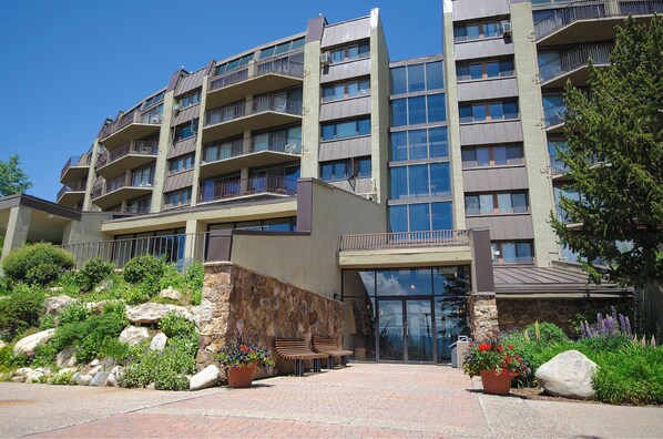 A multi-story hotel with balconies, a stone facade, and a landscaped entrance with benches and potted plants.